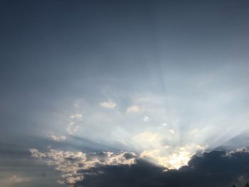 Low angle view of sunlight streaming through clouds