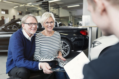 Happy senior couple looking at salesman in car showroom