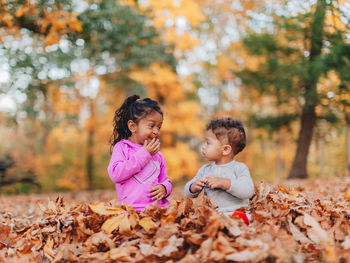 Smiling kids sitting on autumn leaves outdoors