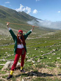 Woman with arms raised standing on landscape against mountain range