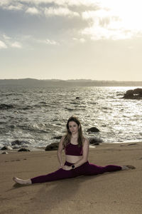 Beautiful young woman doing the splits on the beach in front of the sea