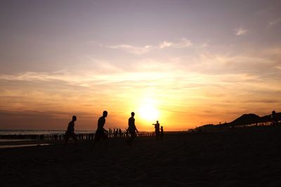 Silhouette people on beach against sky during sunset