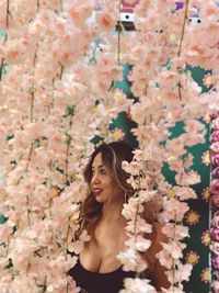 Smiling woman standing amidst pink flowers while looking away