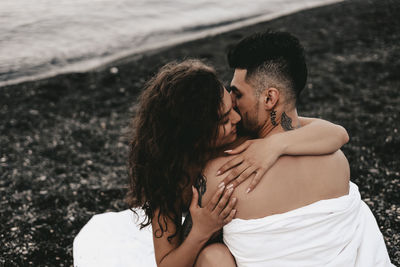 A diverse of lovers a man and a woman embrace under a blanket on the ocean at night outdoor