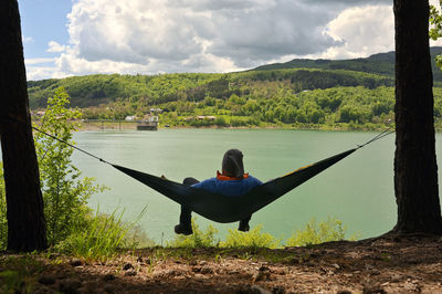 Rear view of man sitting on riverbank against sky