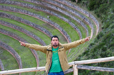 Portrait of young man with arms outstretched standing against amphitheater