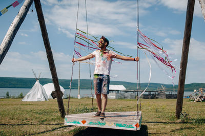 Man standing on swing over land against sky