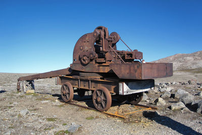 Abandoned car on land against clear blue sky