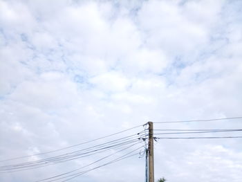 Low angle view of electricity pylon against cloudy sky