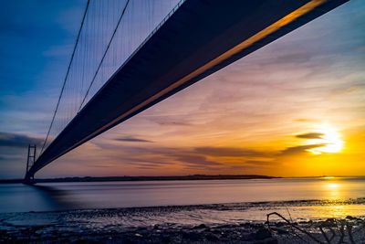 Suspension bridge over sea against sky during sunset