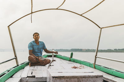 Portrait of young man sitting on boat against sky