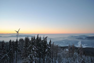 Windmill in forest against sky during sunset