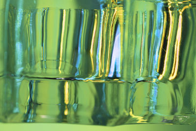 Abstract close up of a glass object with green and blue lights creating colorful stripes.