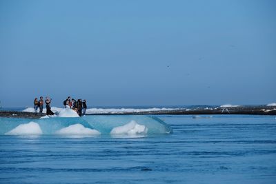 People on sea against clear blue sky