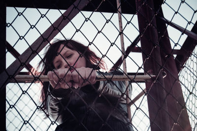 Low angle view of woman standing on chainlink fence