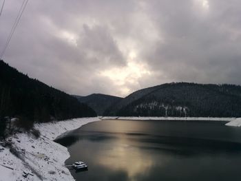 Scenic view of frozen lake and mountains against cloudy sky