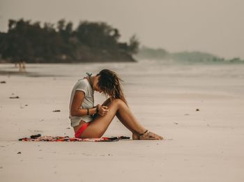 Woman sitting on beach against sky