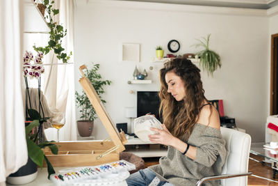 Woman mixing colors sitting on chair in living room at home