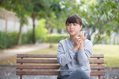 Young woman scratching hand while sitting on bench at park