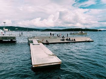 People on pier at sea against sky