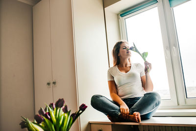 Young woman looking through window at home