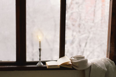 Cup of hot tea and an open book with a warm sweater on a vintage wooden windowsill