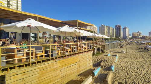 People on beach by buildings against clear sky