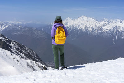 Rear view of man standing on snowcapped mountain against sky