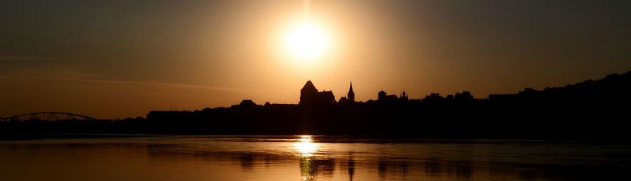 Silhouette of buildings at waterfront during sunset
