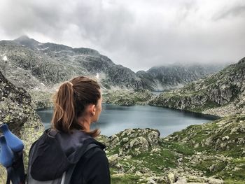 Woman looking at lake and mountains against cloudy sky