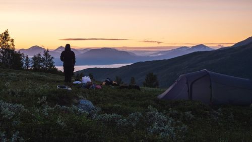 Rear view of man standing on mountain against sky during sunset