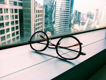 Close-up of eyeglasses on window sill against buildings in city