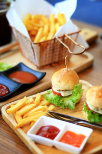 Burgers with tomato, lettuce, cucumber, french fries,onion and cheese on a wooden board