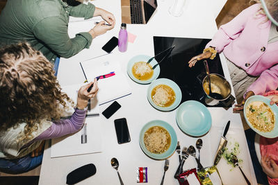 High angle view of multiracial young friends having noodles while studying at dining table in college dorm