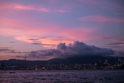 Sea by buildings against sky at sunset