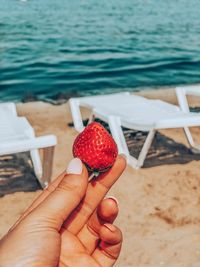 Midsection of person holding strawberry at beach