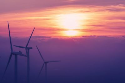 Silhouette of wind turbines against orange sky