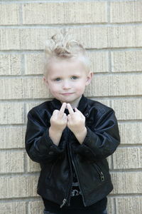 Portrait of cute boy showing middle finger against brick wall