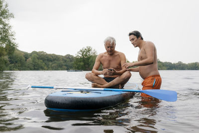 Older and younger man with sup board on a lake using cell phone