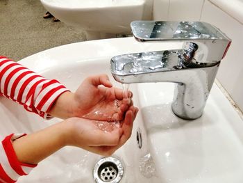 Cropped hands under running water in bathroom