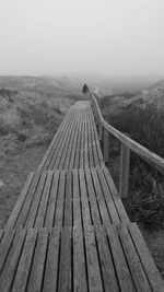 Rear view of man walking on boardwalk against mountain