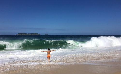 Rear view of woman standing on shore against sea at beach