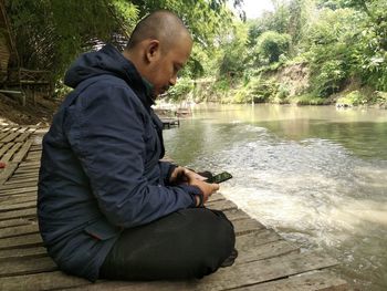 Side view of man sitting on chair at lake