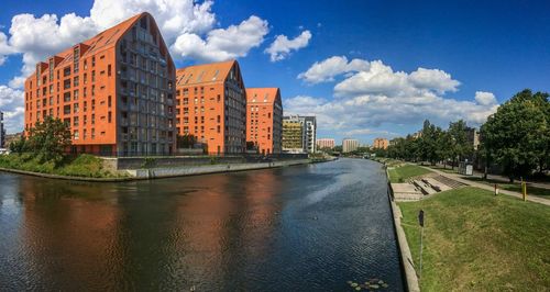 View of buildings by river against cloudy sky