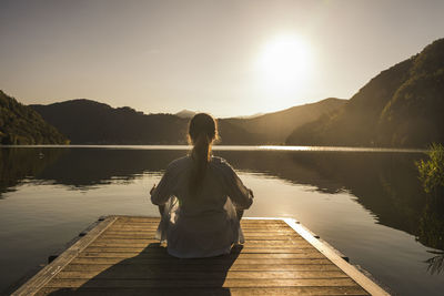 Woman meditating on jetty over lake at vacation