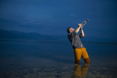 Man playing trumpet while standing in sea at night