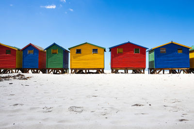 Beach huts by buildings against blue sky