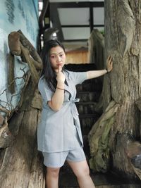 Beautiful young woman standing by tree trunk