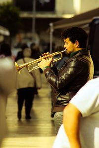 Side view of mature man playing trumpet on footpath at night
