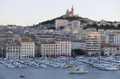 Boats moored in river by buildings in city against clear sky